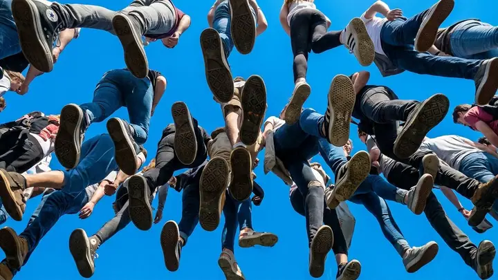 View from below of people walking on transparent glass against a blue sky