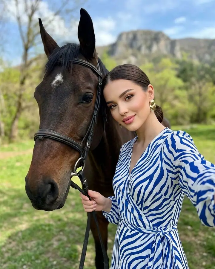 Woman in a striped dress taking a selfie cheek to cheek with a horse