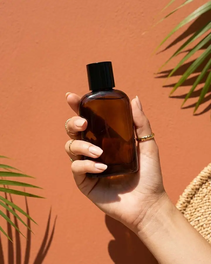 AI example of a hand holding an amber perfume bottle against a terracotta wall