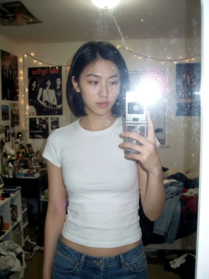 AI example of a grainy 2000s mirror selfie of a woman with a flip phone and flash flare